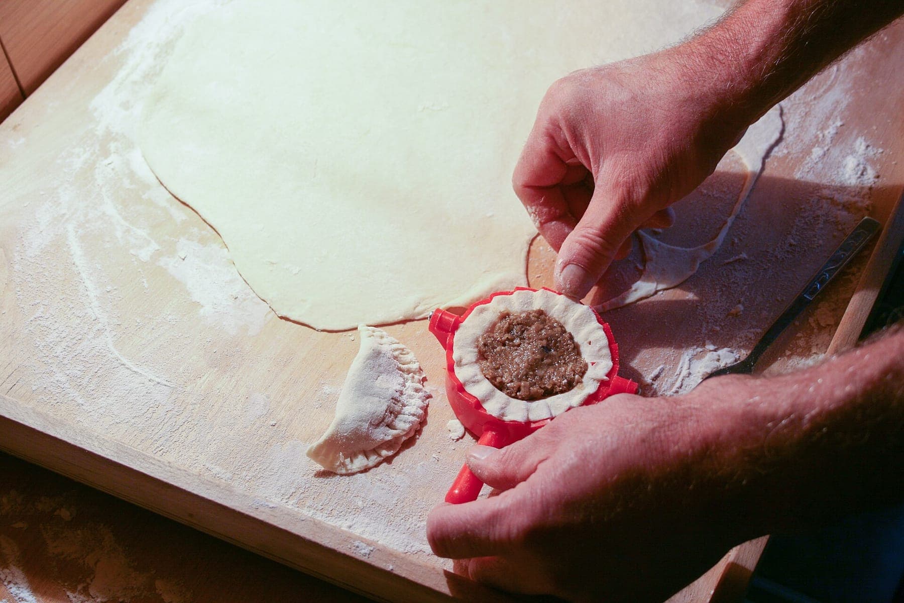 Hands folding pierogi dough on a floured wooden board