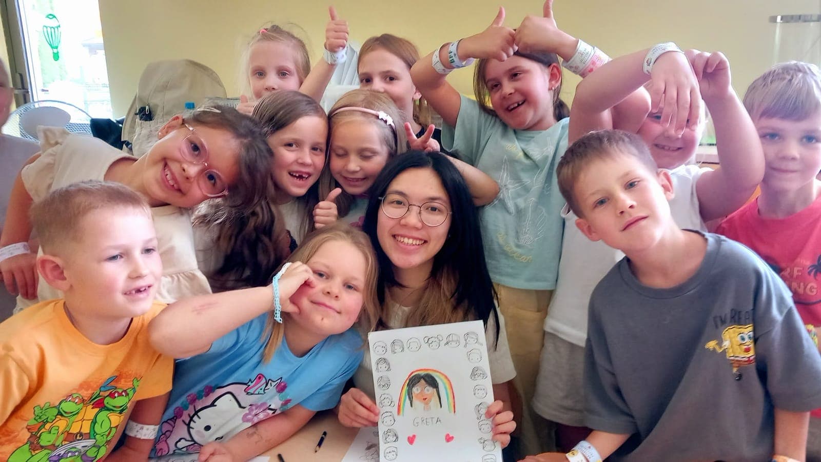 An exchange participant surrounded by laughing children holding up a hand-made card